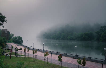 Empty pedestrian street along river at rainy foggy evening.の写真素材