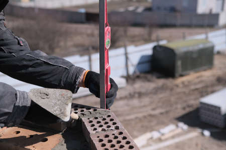 industrial worker building exterior walls, using level for laying bricks in cement. Detail of worker with tools.の写真素材