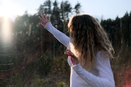 Girl catching sunrays with hand. Young Caucasian woman with stretched hand standing outdoors in the forestの写真素材