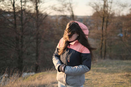 Zhytomyr, Ukraine - April 5, 2021: Portrait of young woman in winter jacket with hair blowing in the wind. Nature and forest background. Wanderlust autumn travel, atmospheric moment.のeditorial素材