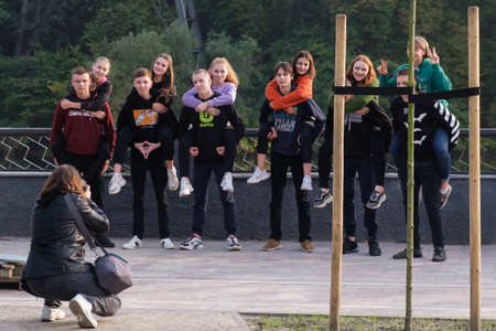 Zhytomyr, Ukraine - October 11, 2020: Happy couples friends men women posing for a photographer. Boyfriends give piggyback ride to girlfriends. Girls sit on mens back over river bank in summer dayのeditorial素材