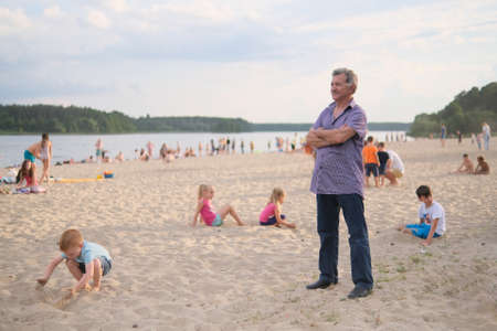 Zhytomyr, Ukraine - July 6, 2021: Man watching for children playing on the sand beach. The man makes sure that the children do not drownのeditorial素材