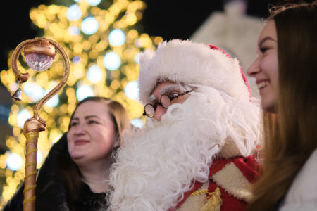 Zhytomyr, Ukraine - December 19, 2021: Santa Claus at Christmas market hugs girls at night.のeditorial素材