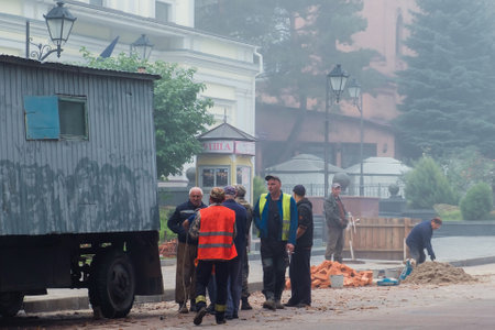 Zhytomyr, Ukraine - May 25, 2021: Road workers, road works, digging hole at asphalt and changing sewers at foggy weather.のeditorial素材