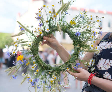 The girl makes a wreath at the head. The process of weaving a wreath with herbs and wild flowers. Summer. Springの写真素材