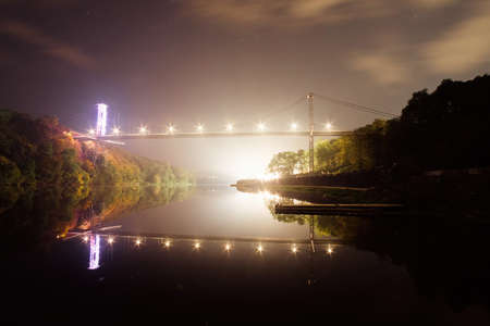 Illuminated pedestrian bridge above river at night park. Building materials for reconstruction river...