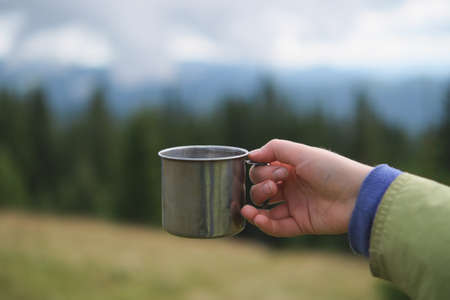 Young woman holding iron mug with hot tea at mountains background.の写真素材