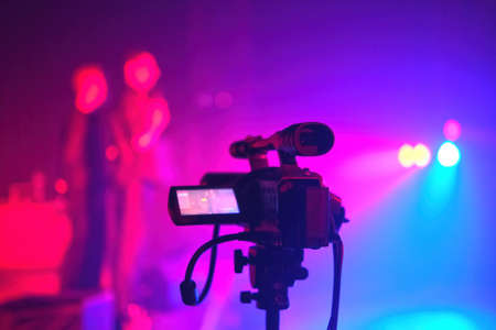 Silhouette of a TV camera, live concert, the shining stage blue light on the theatrical smoke...