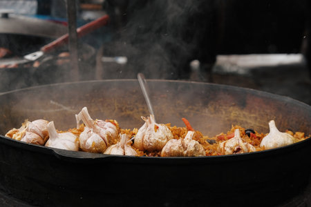 Cooking pilaf rice in a large cast iron pot over the fire. Garlic bulb and red hot pepper.の写真素材