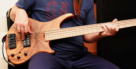 A close up of a man playing a 5 string electric bass guitar.