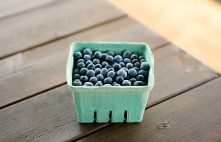 A small basket of freshly picked blueberries on a wooden table.