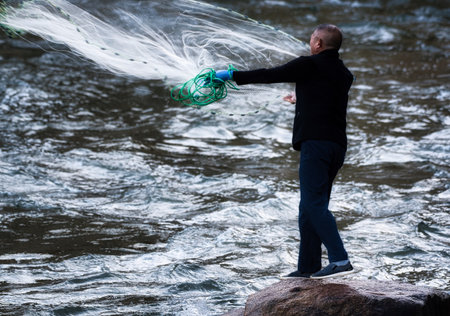 Fisherman with fishing net on a rock in the river.