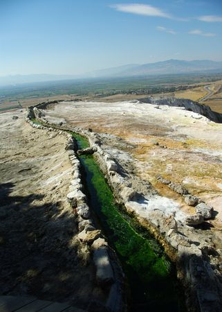 Non-typical Pammukale landscape with green artificial brook outgoing into the distance, and hazed mountains in the horizon (blue sky)の写真素材