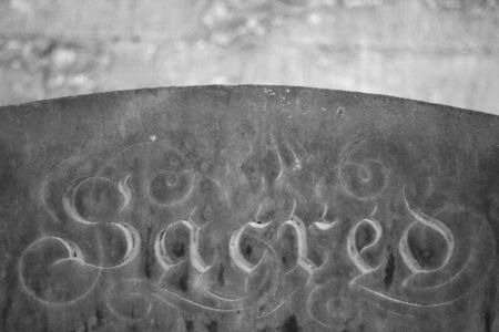 black and white image of a grave stone with the word "sacred" lot of stone texture visibleの写真素材