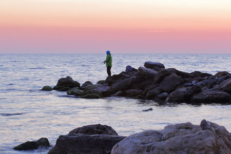 fisherman silhouette on the rocks against the background of sunset over the seaの写真素材