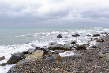 the rocky shore of the undulating sea in cloudy weatherの写真素材