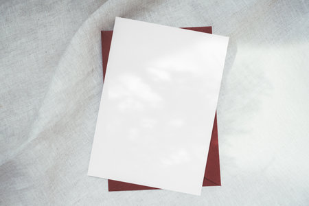 Blank paper card mockup 5x7 with red envelope holiday christmas greeting card postcard on white fabric background with copy space for textの写真素材