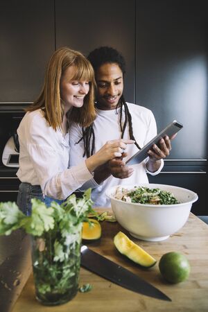 multiracial couple cook vegetarian food, consult cooking recipe with a tablet