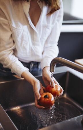 Today's young woman washes tomatoes in a modern kitchenの写真素材
