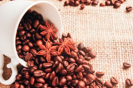 White cup with spilled coffee beans and anise on sackclothの写真素材