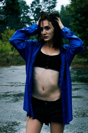 Girl in a blue shirt in the rain amid the wet asphaltの写真素材