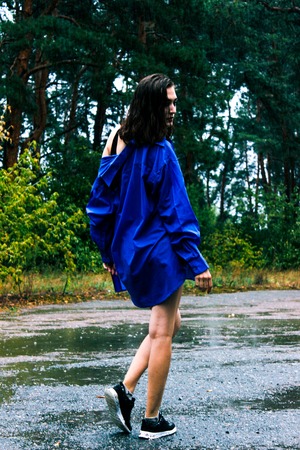 Girl in a blue shirt in the rain amid the wet asphaltの写真素材