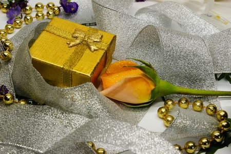 a golden gift box and a rose wrapped in silver ribbon and small purple flowers. side viewの写真素材