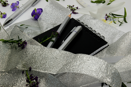 a notebook and gray pens on small purple flowers and a silver ribbonの写真素材