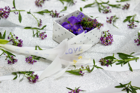 The box is filled with purple flowers on the surface covered with small purple flowers and silver ribbonの写真素材
