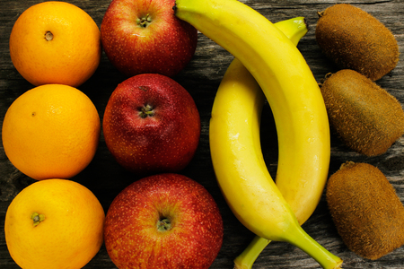 fruit platter of resh mandarins, kiwi and red apples and bananas on gray wooden table view from aboveの写真素材