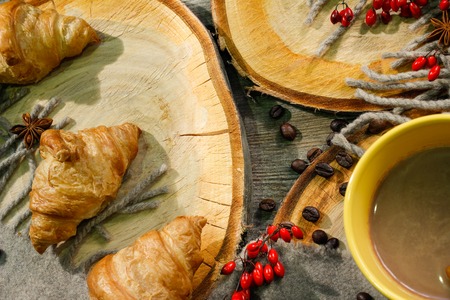 croissants and a cup of coffee on a wooden surface among a woolen blanket and red berries. Autumn motiveの写真素材