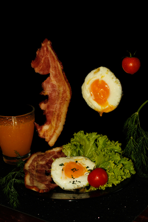Full English breakfast with scrambled eggs in a frying pan, bacon, sausage, beans, tomatoes and juice. Black backgroundの写真素材