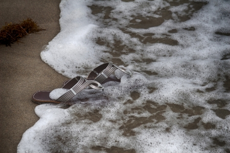 Sandals on the beach are dampened by a wave 