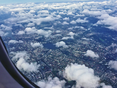 Flying above white cumulus clouds in an airplane with the wingtip and vapor trail visible in a sunny blue sky in a transport conceptの写真素材
