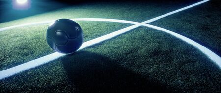 Sports field with football or soccer ball standing on the white lines illuminated from behind by...
