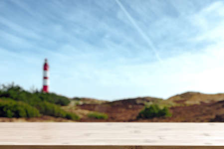 Empty wooden bar on bottom and blurred view of seaside landscape with red-white striped lighthouse. Summer sunny day at sea coast.の写真素材