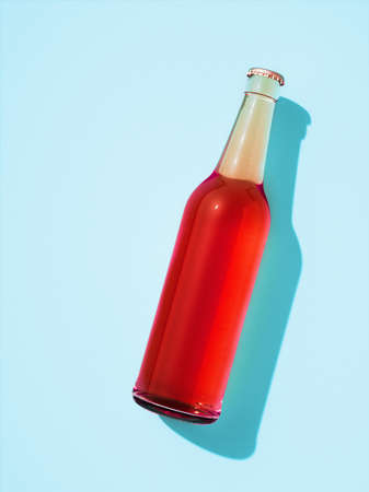 One transparent glass bottle with metal cap laying on light blue surface. Beer bottle full of red drink without label. Retro drink bottle concept.の写真素材