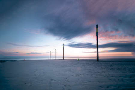 Several tall wooden poles with yellow stripe for marking coastline. Sunset sky with colorful clouds. Long exposure.の写真素材
