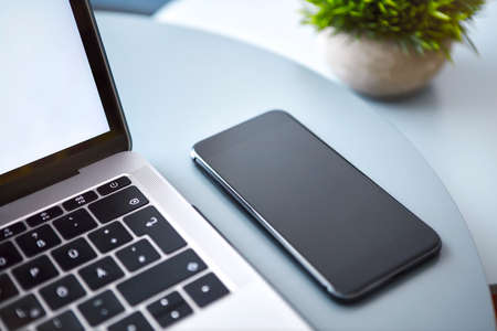 Modern smartphone with rounded edges laying next to laptop on blue round table. Modern technology, wireless device and transfer of energy concept.の写真素材