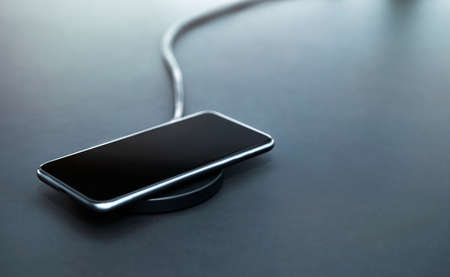 Recharging smartphone battery during workday in office. Using induction wireless charging. Gray background. Modern technology, wireless device and transfer of energy concept.の写真素材