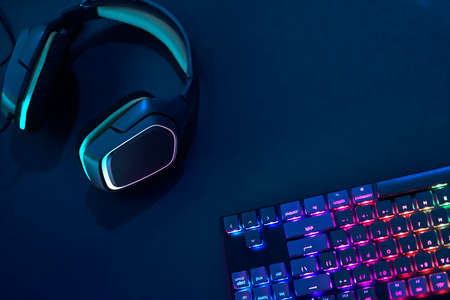 Headphones laying on desk next to rainbow colors backlighted gaming computer keyboard. Professional computer game playing, esport business and online world concept.の写真素材