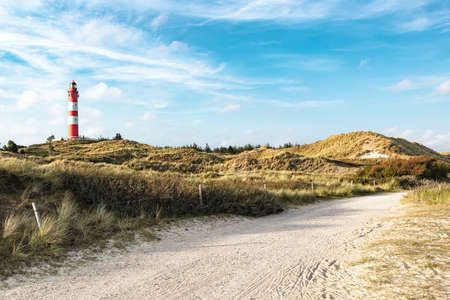 Summer evening view on maritime lighthouse and sandy grassy landscape around. Sandy dirt road for bikers and walkers in foreground.の写真素材