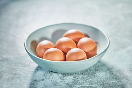 Several brown eggs in porcelain bowl laying on textured concrete rustic background. Selective focus.の写真素材