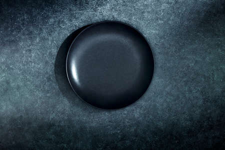 High angle view of black glossy plate standing on dark textured rustic background. Place for add your objects.の写真素材