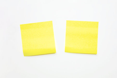 Two Bright Yellow Sticky Notes Are Placed on Smooth White Background. Offer a Clear and Vibrant Option for Jotting Down Reminders or Organizing Thoughts.の写真素材