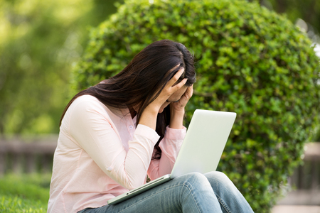 Young beautiful woman working outdoor in a public park. Working on laptop outdoors. Cropped image of female working on laptop while sitting in a park.の写真素材