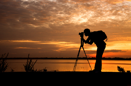 Silhouette Handsome Photographer take a photo with professional camera on the sunset.