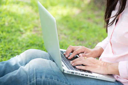 Young Asian beautiful woman with smiling face working outdoor in a public park. Working on laptop outdoors. Cropped image of female working on laptop while sitting in a park.の写真素材