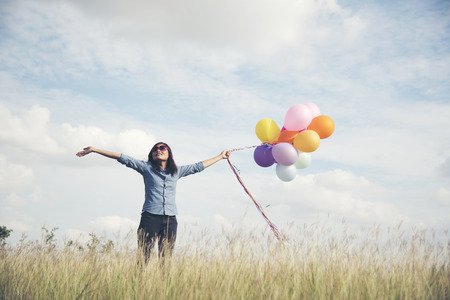 Happy woman holding colorful of balloons on a green meadow with cloudy and blue skyの写真素材