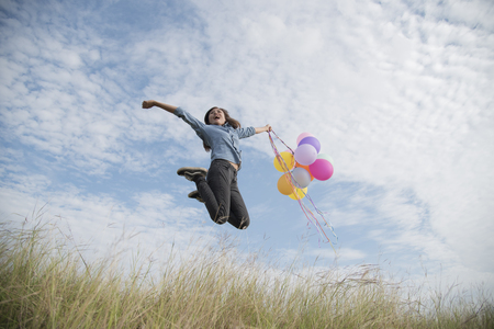 Happy woman jumping with air balloons on the meadowの写真素材